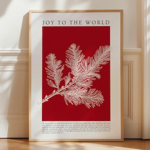 May include: A framed art print with the words "JOY TO THE WORLD" at the top. The print features a red background with a white illustration of a pine branch. Below the illustration is a block of text.