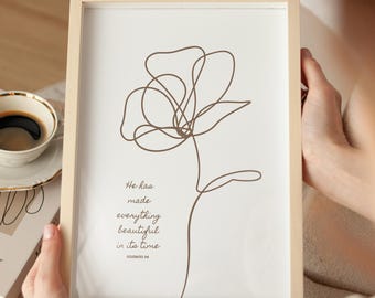 May include: A framed print featuring a minimalist line drawing of a flower in brown against a white background. The print includes the text "He has made everything beautiful in its time." The frame is light wood.