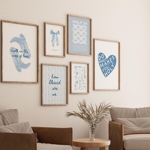 May include: A selection of framed art prints with blue and white designs. The prints feature text and illustrations, including cowboy boots, a bow, and a heart. The frames are light brown, and the art is displayed on a cream wall.