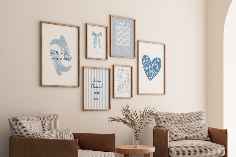 May include: A selection of framed art prints with blue and white designs. The prints feature text and illustrations, including cowboy boots, a bow, and a heart. The frames are light brown, and the art is displayed on a cream wall.