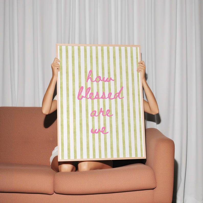 K&ouml;nnte beinhalten: Ein gerahmter Druck mit gr&uuml;nen und wei&szlig;en Streifen und dem Text "how blessed are we" in rosa Kursivschrift.