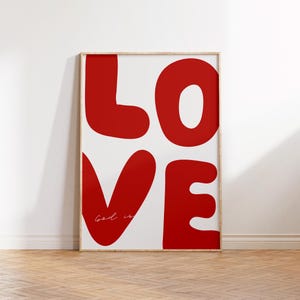 May include: A white framed poster with the word "LOVE" in large, red, stylized letters. The word "God is" is written in cursive in the lower left corner of the poster.