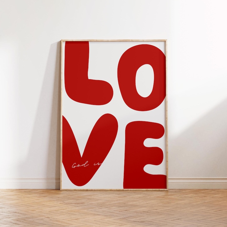 May include: A white framed poster with the word "LOVE" in large, red, stylized letters. The word "God is" is written in cursive in the lower left corner of the poster.