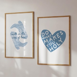 May include: Two framed art prints with light wood frames. One print features blue cowboy boots with the text "walk in the way of love." The other print has a blue heart with the words "do what makes you holy."