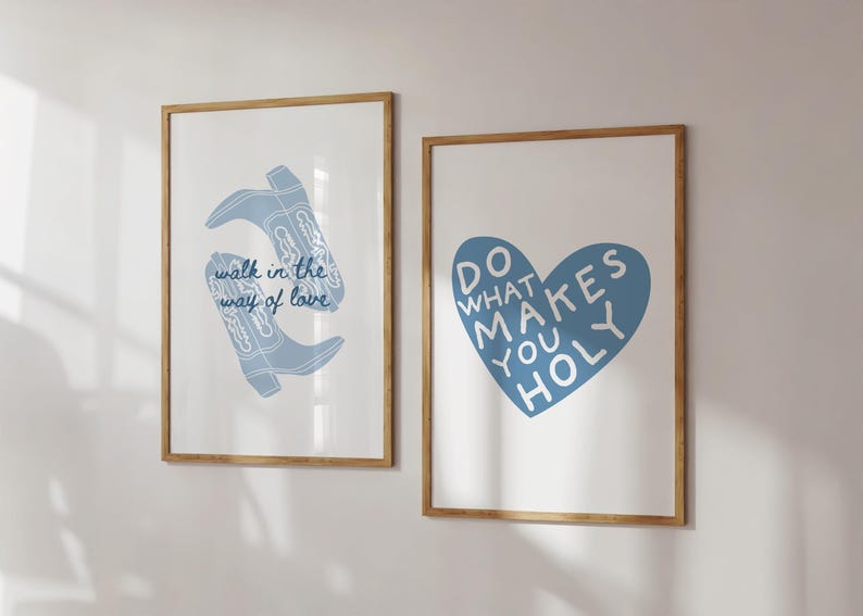 May include: Two framed art prints with light wood frames. One print features blue cowboy boots with the text "walk in the way of love." The other print has a blue heart with the words "do what makes you holy."