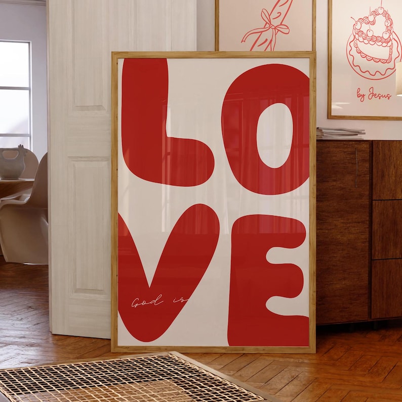 May include: A framed print with the word "LOVE" in large, red, stylized letters. The letters are outlined in white and the background is white. The text "Good is" is written in cursive in the lower left corner of the print.