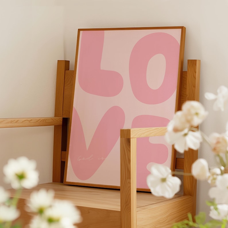 May include: A framed pink and white print with the word "LOVE" in large, stylized letters. The letters are pink and have a slightly puffy appearance. The background is a light pink.