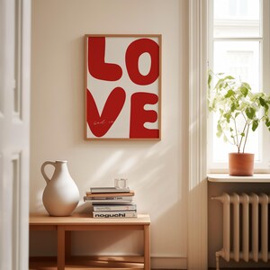 May include: A framed print with the word "LOVE" in large, red, stylized letters. The letters are outlined in black and the background is white. The text "God is" is written in a smaller font below the word "LOVE".