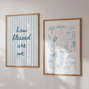 May include: Two framed prints with wooden frames on a wall. One has blue vertical stripes and the text "how blessed are we." The other print has blue line drawings of beach and western themed items.