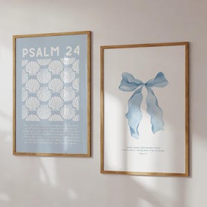 May include: Two framed art prints. One features the text "PSALM 24" above a pattern of white seashells on a light blue background. The other print displays a watercolour image of a blue bow. Both are in wooden frames.