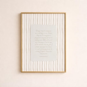 May include: A framed print with a gold-colored frame. The artwork features a light gray paper with handwritten text, set against a background of vertical beige and white stripes. The text is in a script font.