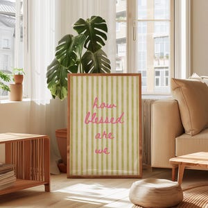 K&ouml;nnte beinhalten: Ein gerahmter Druck mit einem gr&uuml;n-wei&szlig; gestreiften Hintergrund und dem Text "how blessed are we" in rosa.