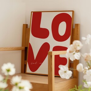 May include: A framed print with the word "LOVE" in large, red, stylized letters. The word "God is" is written in cursive below the letters.