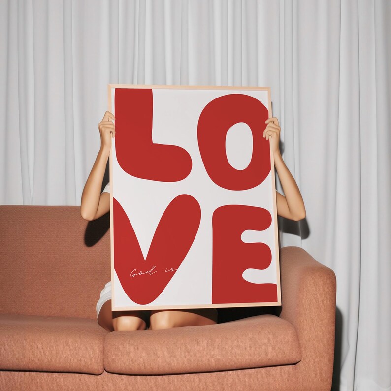 May include: A framed print with the word "LOVE" in large, red, stylized letters. The letters are outlined in white. The word "God is" is written in white script inside the heart-shaped letter "V".