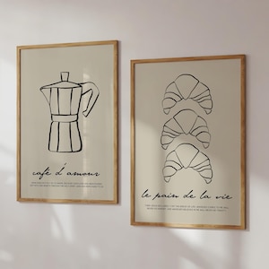 Könnte beinhalten: Zwei gerahmte Drucke mit schwarzen Strichzeichnungen. Der linke Druck zeigt eine Kaffeekanne mit dem Text "cafe d'amour". Der rechte Druck zeigt drei übereinander gestapelte Croissants mit dem Text "le pain de la vie".