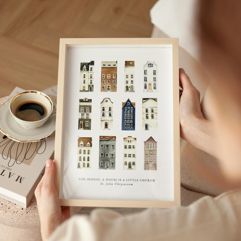 May include: A framed print featuring watercolor illustrations of various houses in a grid pattern. The houses are in different colors and architectural styles. The text "FOR INDEED, A HOUSE IS A LITTLE CHURCH St. John Chrysostom" is at the bottom.