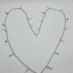 Puede incluir: Un collar de cadena de plata con múltiples dijes, incluyendo llaves, un martillo, un cuchillo y un abridor de botellas.