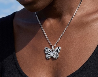 May include: A silver-toned necklace featuring a butterfly pendant with cut-out wing details and small, circular, textured accents on the upper and lower wing sections, suspended from a simple, polished silver-toned metal chain link necklace.