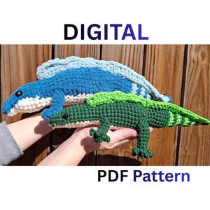 May include: Two crocheted lizard toys, one blue and one green, are displayed. The blue lizard has a light blue spine, and the green lizard has a green and lime green spine. The text "DIGITAL" and "PDF Pattern" are displayed in the image.