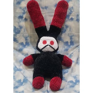 May include: A black and red crocheted plush bunny with large red button eyes. The bunny has a white face with a black stitched mouth.