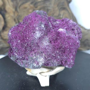 May include: A raw mineral specimen featuring a vibrant, deep magenta crystalline surface with a porous, textured appearance. The stone displays a mix of intense purple hues and darker, greyish-black mineral inclusions across its irregular, jagged form.