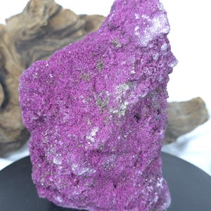 May include: A rough, jagged mineral specimen with a vibrant magenta and purple crystalline surface. The rock features a porous, uneven texture with small, sparkling metallic flecks embedded throughout the deep pink and violet mineral formation.