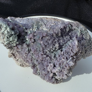 May include: A large, irregular-shaped rock formation with a bubbly, grape-like texture. The rock features a mix of colors, including shades of lavender, gray, and hints of green. The surface is covered in small, rounded nodules, creating a unique, organic appearance.