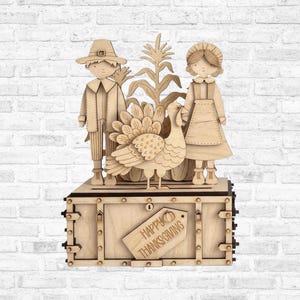 May include: A laser-cut wooden Thanksgiving decoration featuring a pilgrim figure, a bonneted figure, and a turkey standing atop a rectangular chest. The chest is adorned with a wooden tag engraved with the text Happy Thanksgiving and a pumpkin icon.