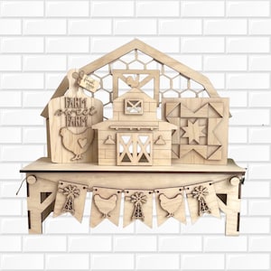 Könnte beinhalten: Ein helles Holz-Etageren-Display mit einem scheunenförmigen Hintergrund, einem Schneidebrett-Schild mit der Aufschrift Farm Sweet Farm und einem kleinen Anhänger mit fresh eggs, einer zentralen Scheune, einem Quilt-Block und einem Banner mit Windmühlen.