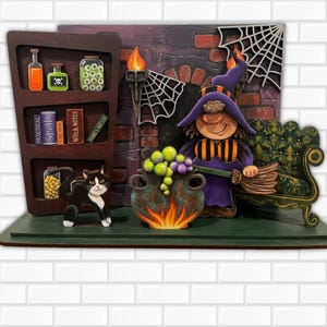 Op de afbeelding: Een gelaagde houten Halloween-decoratie met een heks in een paarse hoed die een bezem vasthoudt, een ketel met groene en paarse bubbels, een zwart-witte kat en een plank met toverdrankflesjes en boeken met de titel Practical Spells.