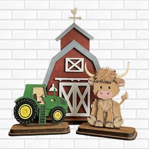 May include: A layered wooden decorative set featuring a red barn with a gray roof and a weather vane, a green tractor with yellow wheels, and a tan Highland cow with long horns. Each piece is mounted on a separate dark brown wooden base.