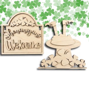 May include: Two wooden St. Patrick's Day decorations. One is a sign that says "Shenanigans Welcome" with shamrock accents. The other is a leprechaun hat with shamrocks at the base. The background has a pattern of green shamrocks.
