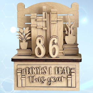 May include: A wooden bookshelf-style display with the number "86" in the center. The display includes cut-out book and plant designs, and the text "#BOOKS I READ this year". The piece is made of light-colored wood.