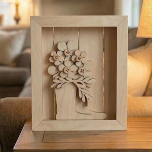 May include: Wooden framed wall art featuring a laser-cut design of flowers in a boot. The flowers are adorned with brown button centers. The artwork is made of light-colored wood and is displayed on a wooden table.