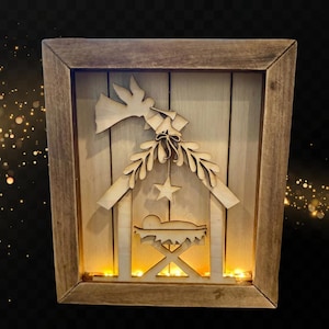 May include: Wooden nativity scene in a framed shadow box. The scene features a dove, star, and a baby in a manger. The frame is made of dark wood, and the scene is illuminated with warm white lights.
