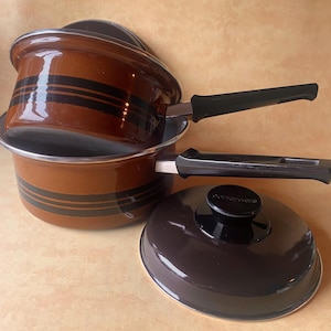 May include: Brown enamel cookware set with black horizontal stripes. The set includes two pots with black handles and a matching lid. The pots have a silver rim and the lid has a black knob. The cookware is likely vintage.