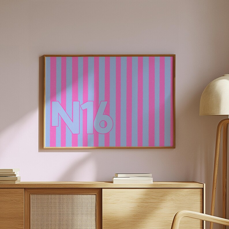 Puede incluir: Una impresi&oacute;n art&iacute;stica enmarcada con un patr&oacute;n de rayas verticales en tonos rosa y azul claro. El texto "N16" est&aacute; centrado en la obra de arte en un color azul claro a juego. La obra de arte se muestra en una pared rosa.