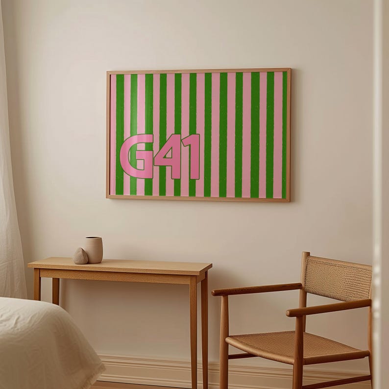 Puede incluir: Una obra de arte enmarcada con un fondo de rayas rosas y verdes y el texto rosa "G41". La obra de arte se exhibe en una pared de color claro, encima de una mesa y una silla de madera. Un jarr&oacute;n est&aacute; sobre la mesa.