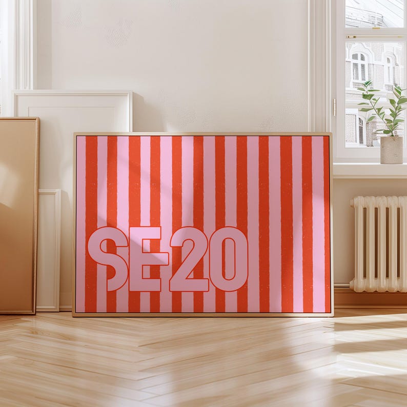 Puede incluir: Una obra de arte enmarcada con un dise&ntilde;o llamativo. Presenta rayas verticales en rojo y rosa. El texto "SE20" est&aacute; en rosa claro. El marco es de color madera clara. La obra se exhibe en interiores.