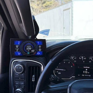 May include: A vehicle interior featuring a black steering wheel with a GMC logo, a digital instrument cluster displaying a fuel range of 113 miles, and a mounted digital performance monitor screen showing various engine data metrics in blue and white.