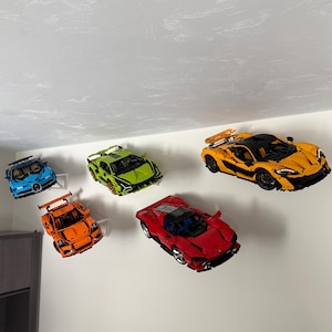 May include: A collection of toy model cars in various colours, including blue, green, orange, red, and yellow. The toy cars are mounted on white brackets against a white wall. The cars are detailed with realistic features.
