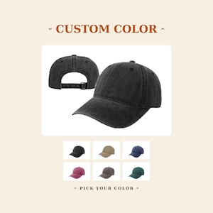 May include: A black baseball cap with a distressed finish, shown from the front and back, featuring an adjustable strap. Below, a grid displays six additional baseball caps in black, tan, blue, maroon, brown, and green with the text CUSTOM COLOR.