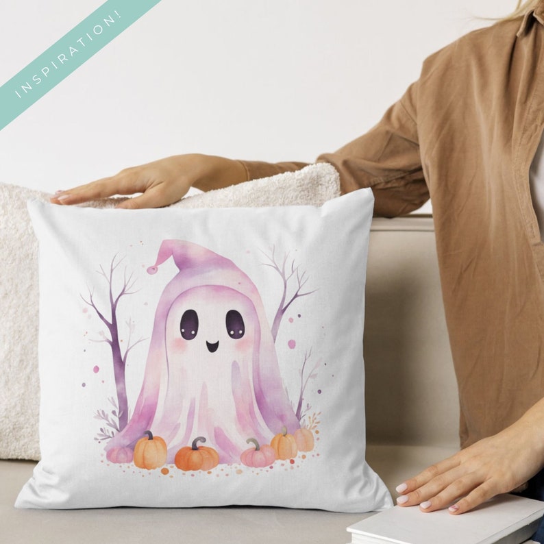 May include: White square pillow featuring a watercolor illustration of a friendly ghost wearing a pink hat. The ghost is surrounded by pumpkins and bare trees, perfect for Halloween decor. The word "INSPIRATION!" is in the upper left corner.