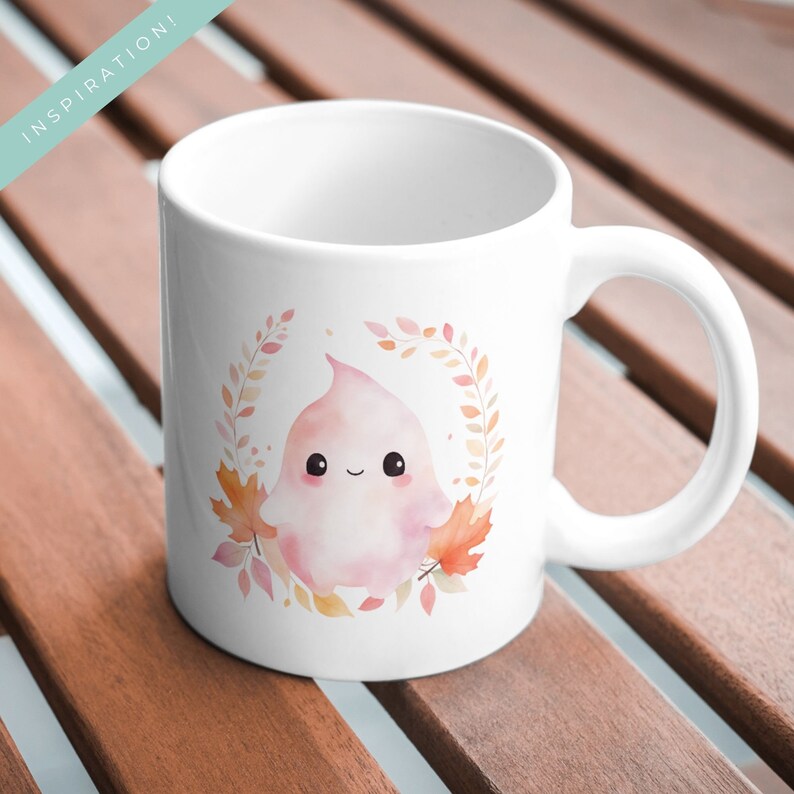 May include: White ceramic mug featuring a cute, pink ghost illustration surrounded by autumn leaves. The ghost has a smiling face. The word "INSPIRATION!" is printed in a teal banner in the upper left corner. The mug has a curved handle.