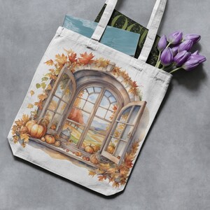 May include: A white canvas tote bag with a watercolor illustration of a window with fall leaves and pumpkins. The window looks out onto a field with trees and a blue sky.