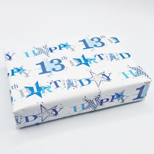 May include: White wrapping paper with a blue and silver pattern of stars and the words "Happy 13th Birthday".