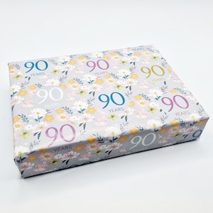 May include: A gray gift wrap with a floral pattern and the number "90" repeated in different colors and fonts. The text "YEARS" is printed below each number.