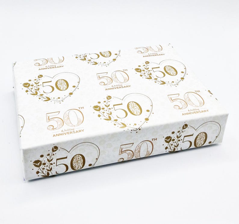 May include: White gift box with a gold pattern of hearts and the text "50th Anniversary" repeated. The box is decorated with gold floral accents.
