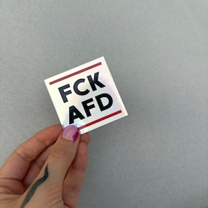Könnte beinhalten: Ein silberner Aufkleber mit roten Linien und schwarzem Text, der "FCK AFD" lautet.