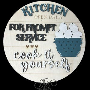 May include: A round wooden sign with the text "Kitchen Open Daily, For Prompt Service, Cook It Yourself" in black and white lettering. The sign also features a blue colander with white eggs inside and two small brown hearts.